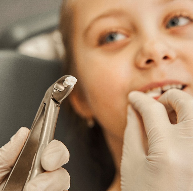 Forceps with extracted tooth in foreground with little girl with gauze in mouth blurry in background