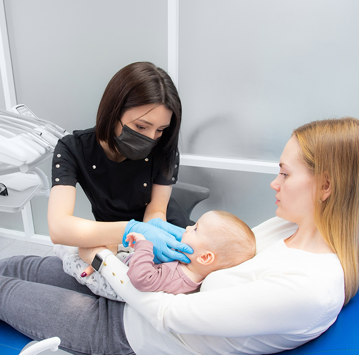 Baby receiving a dental exam while sitting in their mothers lap
