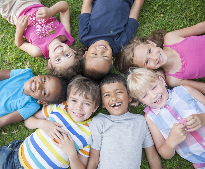 Group of children laying in a circle on grass with their heads together in the middle