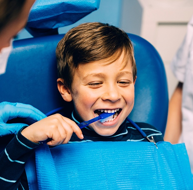 Child smiling while brushing his teeth in office