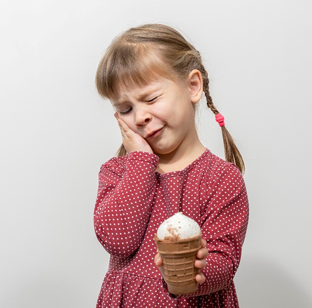 Little girl cringing in pain at tooth sensitivity while holding ice cream