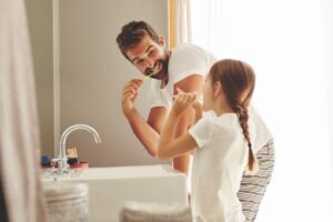 Dad and daughter brushing teeth together.
