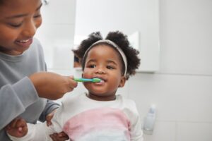 Parent helping child brush teeth.