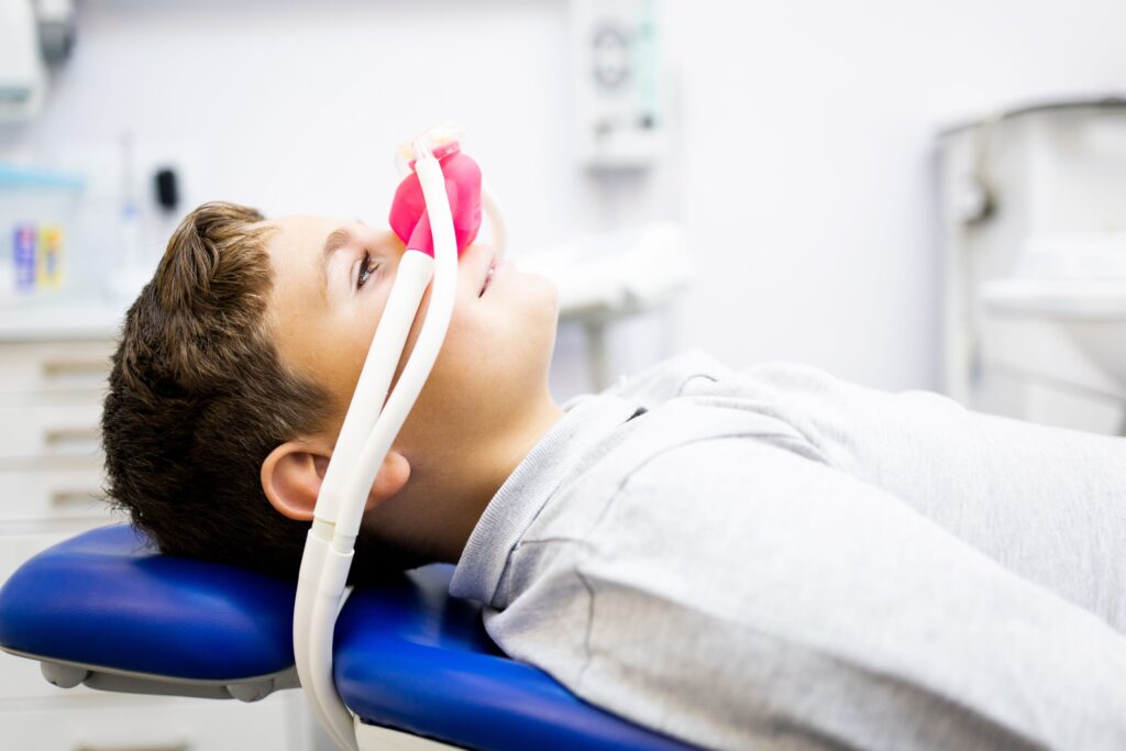 Kid in dental chair with pink laughing gas mask over nose