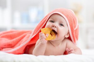 Baby covered with towel, chewing on teething ring.